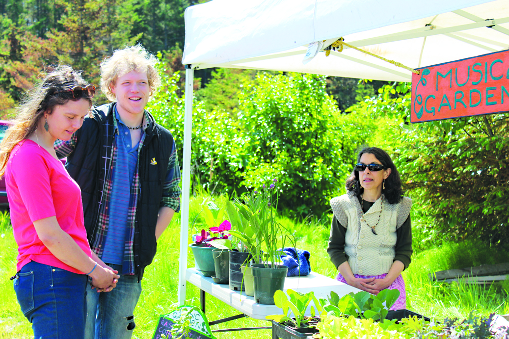 Andy Kellogg and Homer Wilson chat with Lindianne Sarno at her stand, Music Garden, on May 28, the opening day of the Homer Farmers Market. -Photo by Anna Frost, Homer News