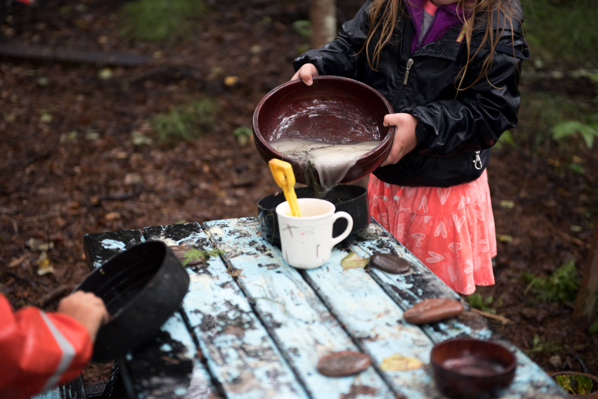 A Tiny Trees student plays in the outdoor play kitchen, pouring water from a bowl into a cup. (Photo by Scott Dickerson)