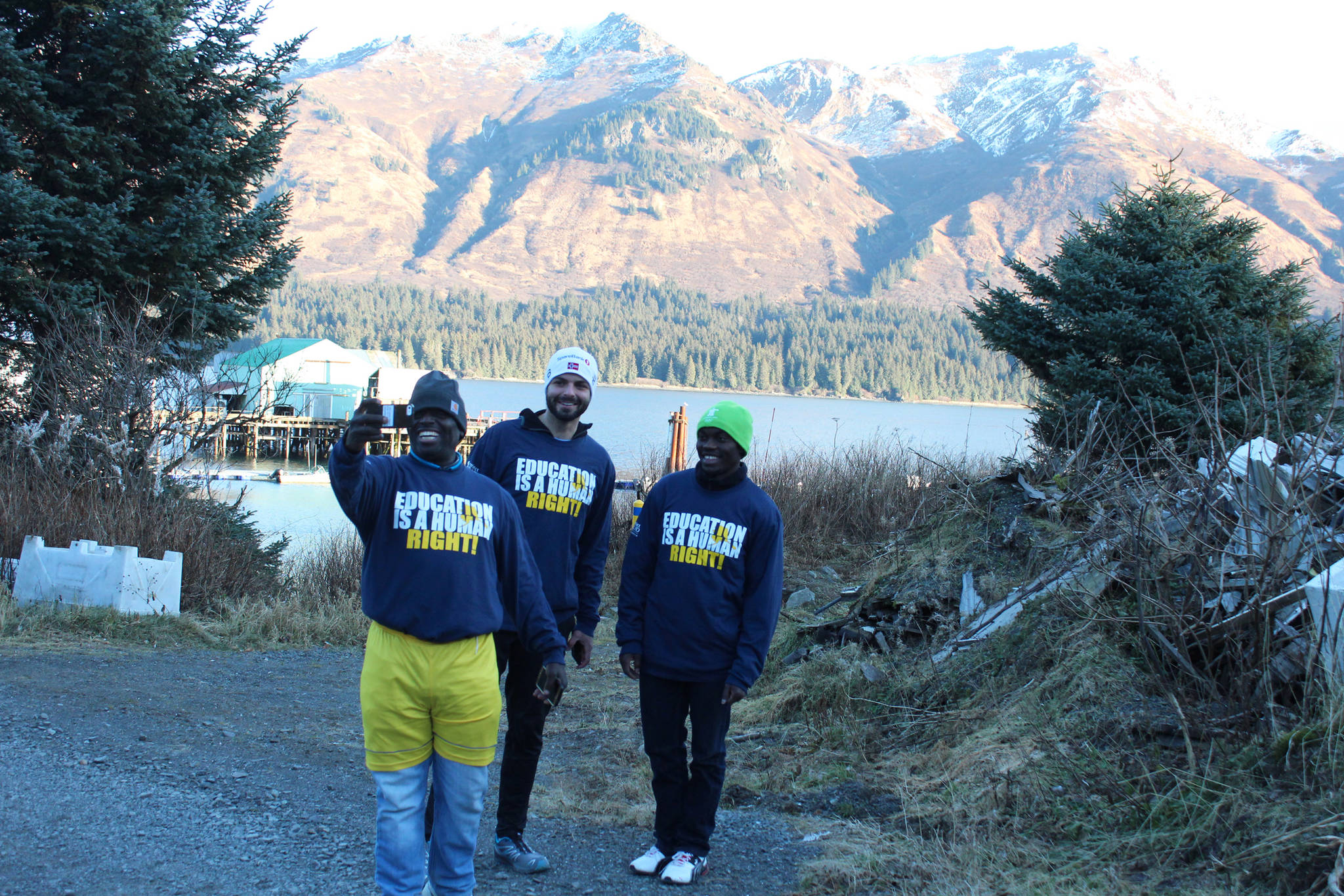 Human rights lawyer and Kenya native Chris Mburu takes a selfie with Kenny Daher of Project GRAD, center, and Kimani Nyambura, right, in front of the mountains Thursday, Nov. 16, 2017 in Port Graham, Alaska. Mburu, who started a foundation to put Kenyan children through school after being sponsored himself, gave presentations to several Kenai Peninsula schools this week along with Nyambura, one of the students who has been able to go to school thanks to the foundation. (Photo by Megan Pacer/Homer News)