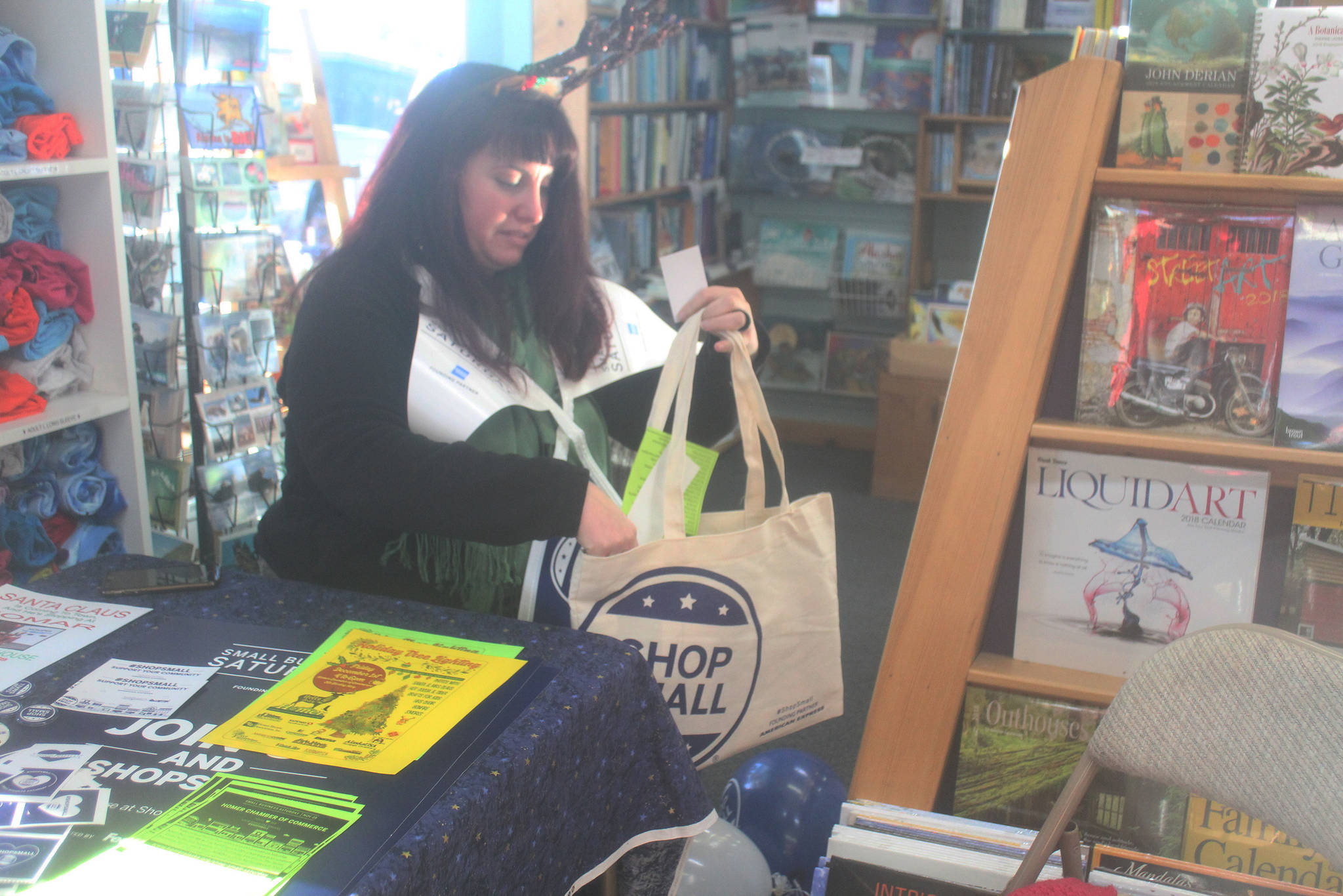 Nyla Lightcap, membership director for the Homer Chamber of Commerce, fills a Shop Small Saturday tote with stickers and information during the local business event Saturday, Nov. 25, 2017 at the Homer Bookstore in Homer, Alaska. (Photo by Megan Pacer/Homer News)