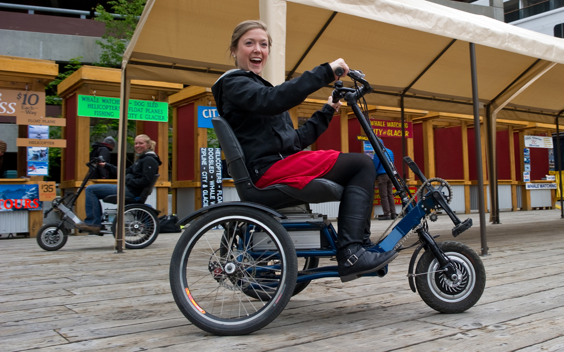 Kellen Priest, right, and Abby Leatherman, both tour brokers for Gastineau Guiding, ride electric-powered tricycles in  downtown Juneau late last month. Bob Janes invented the Access Hybrid, a trike with an assistive electric motor, meant to provide all the fun of a bicycle and all the function of a traditional mobility device. -Photo by Michael Penn, Morris News Service - Alaska