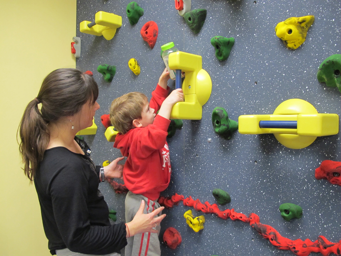 Jackie Forester, pediatric occupational therapist, assists Silas Pyatt-James, 4, as he tackles the climbing wall, which helps children develop physical coordination and strength. -Photo provided