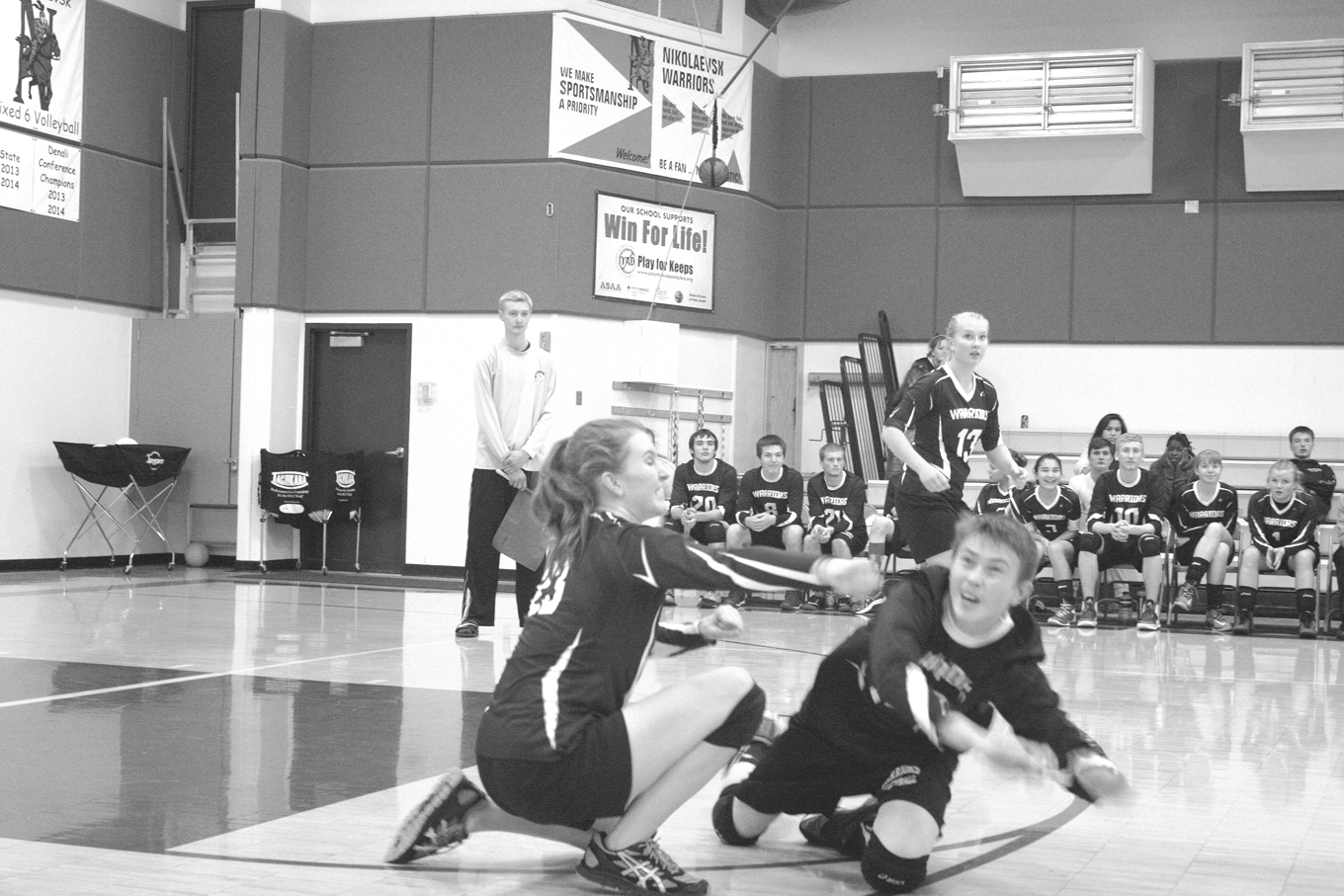 Nikolaevsk senior Serafima Kalugin goes to the ground for a dig with an assist by sophomore Kalenik Molodih. Sophomore Vera Fefelov reacts to support her team.-Photo by Nicetas Lasiter