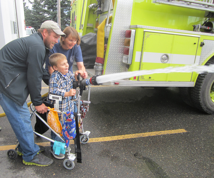 Ethan Beard, center, gets a lesson from Elaine Grabowski of the Homer Volunteer Fire Department on operating a fire hose. Ethan’s dad, Brent, lends a hand. -Photo provided