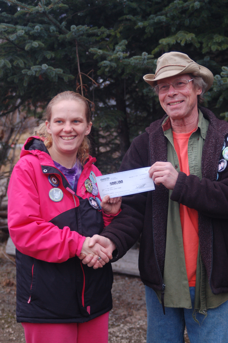 Dax Radtke, right, on Tuesday presents Gail Essex, left, with a $100 check for being one of the winners in the Homer Winter Carnival button contest. Essex bought one of two “opposites attract” winning buttons randomly dispersed among buttons offered for sale around town. Another button may still be out there to be claimed for a $100 prize of gift certificates. There also is a prize for the person who has the most winter carnival buttons and a button with a number written on the back.-Photo by Michael Armstrong, Homer News