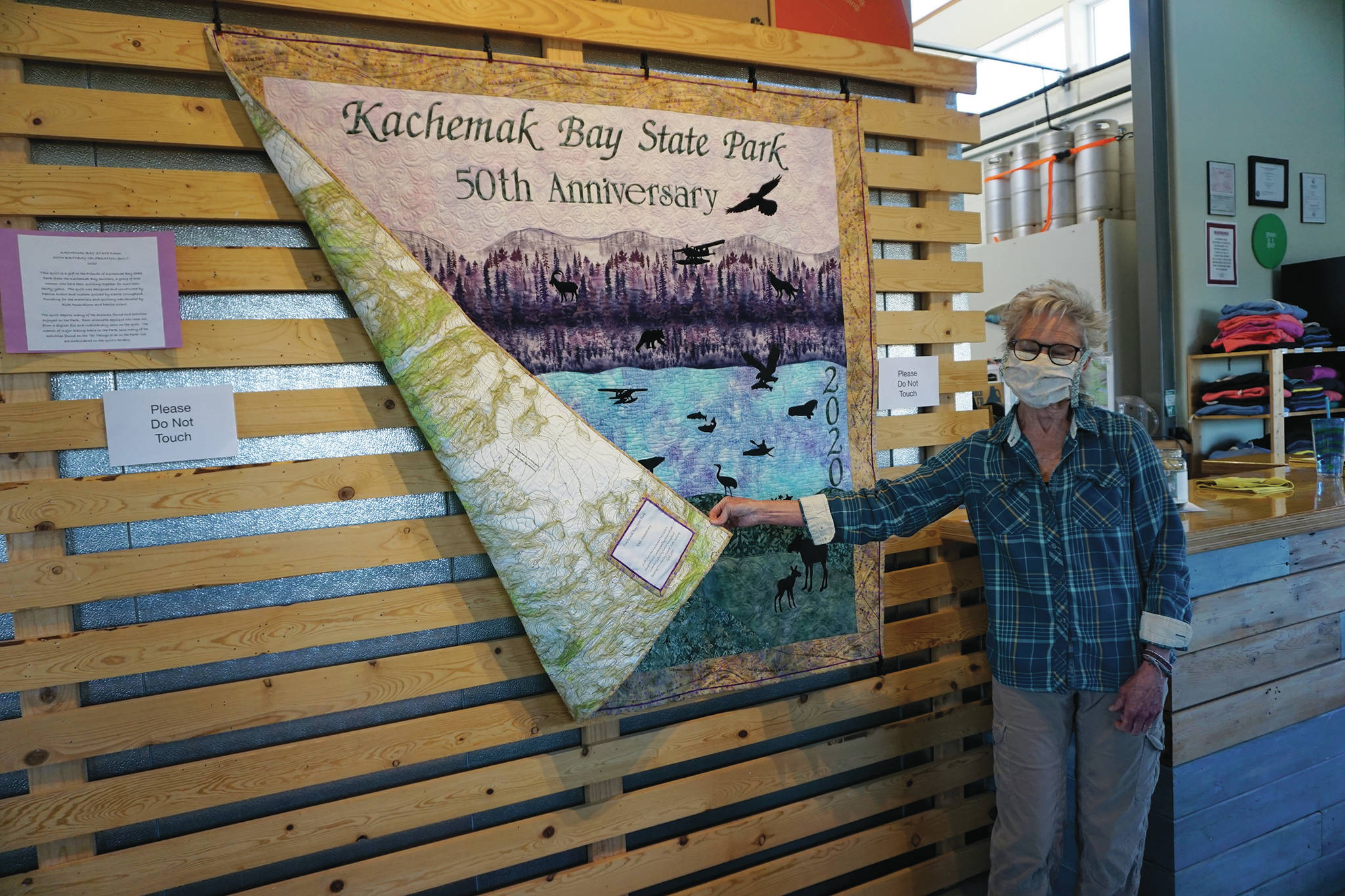 Grace Ridge Brewery co-owner Sherry Stead shows the back side of a quilt by Patrice Krant and Karrie Youngblood commemorating the 50th anniversary of Kachemak Bay State Park on Saturday, May 16, 2020, at Grace Ridge Brewery in Homer, Alaska. Krant designed and sewed the quilt and Youngblood did the quilting. (Photo by Michael Armstrong/Homer News)