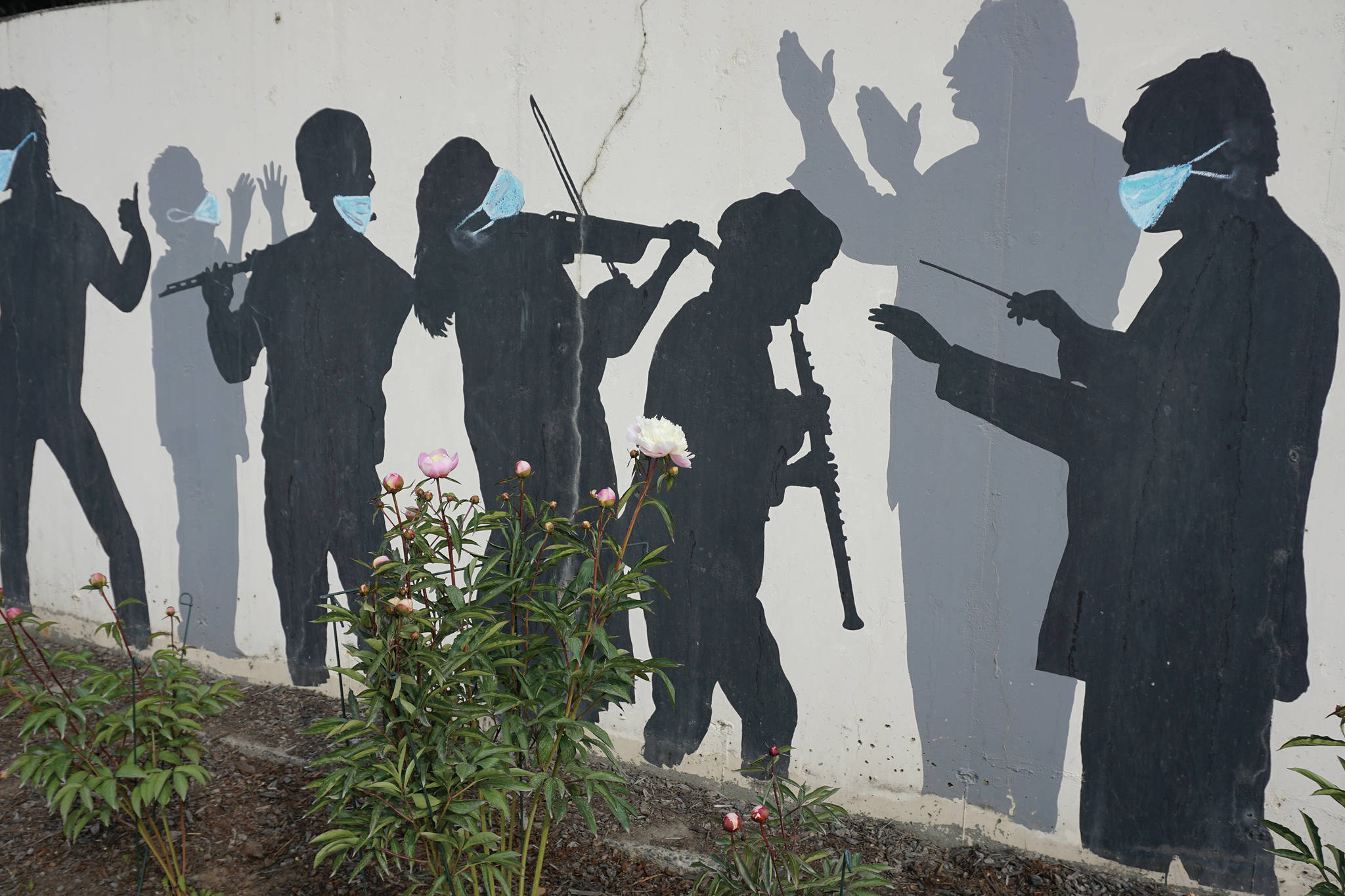 As a reminder to be safe during the COVID-19 pandemic, Homer artist Julie Tomich painted face masks on the figures of Tom Reed’s mural, “Tribute to Performing Artists,” as seen on July 3, 2020, on Pioneer Avenue in Homer, Alaska. Reed painted the mural in August 1985 on a retaining wall in front of NOMAR (then Proctor’s Grocery), and updated the mural with additional figures in 2008 under a city grant. Using a chalk-based, non-permanent paint, Tomich got permission from the city to add the masks to the mural. (Photo by Michael Armstrong/Homer News)