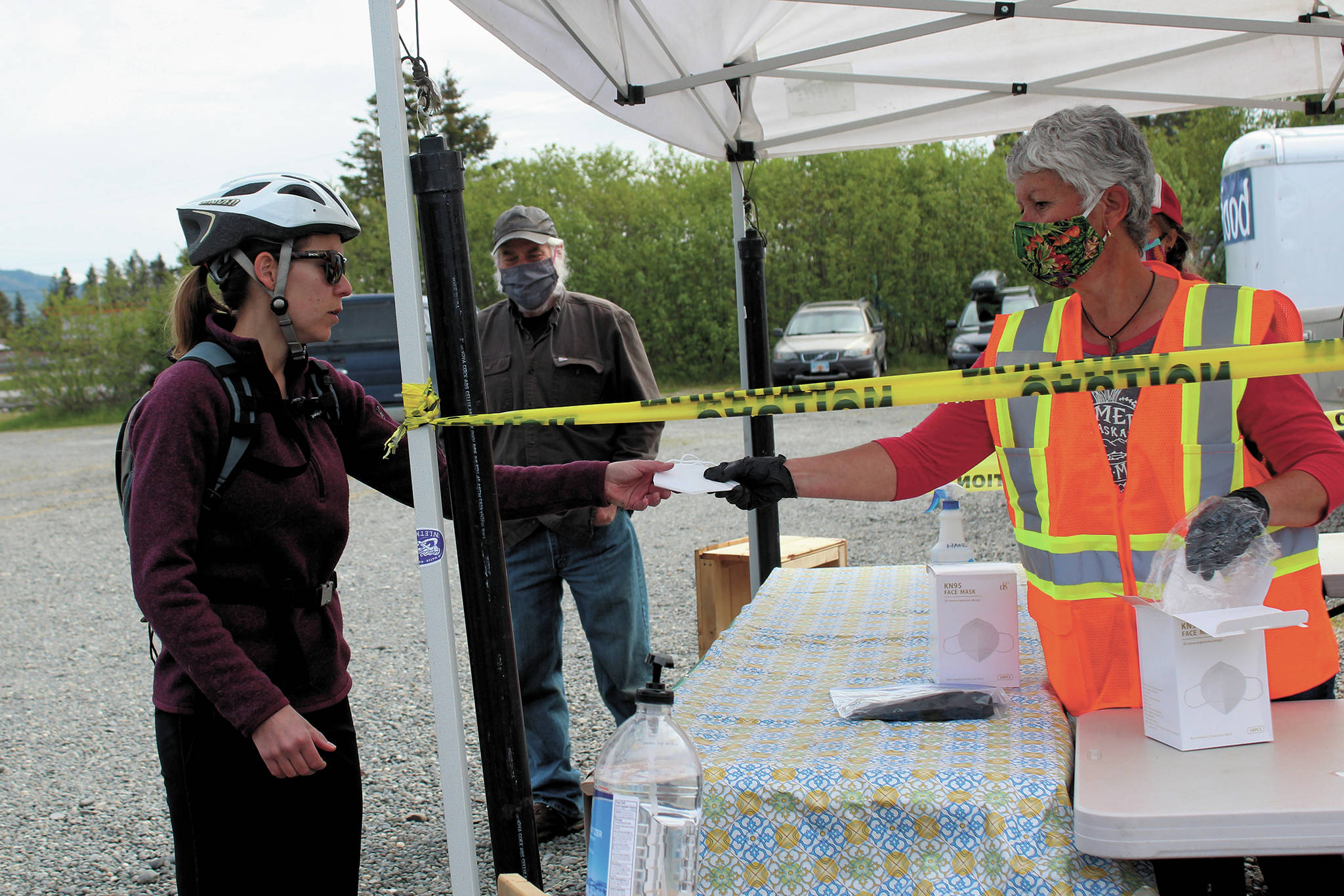 Margarida Kondak, right, hands a visitor a mask before she walks in at the Homer Farmers Market entrance on Saturday, May 30, 2020 in Homer, Alaska. (Photo by Megan Pacer/Homer News)