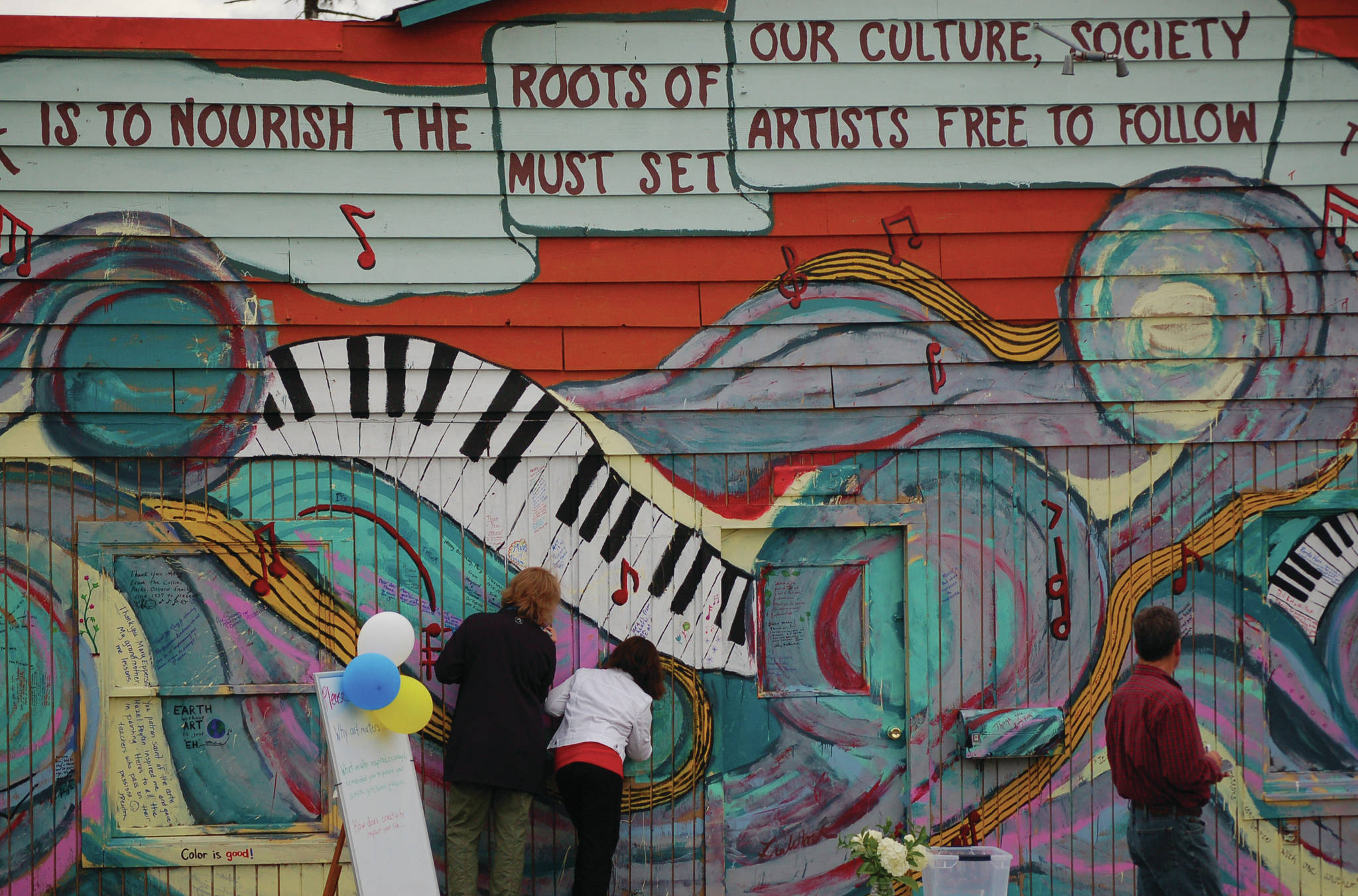 Jenny Martin, left, and Tianah Cavanaugh, center, write on the front of  Etude Studio during Mary Epperson Day on June 6, 2014, in Homer, Alaska. (Photo by Michael Armstrong/Homer News file photo)