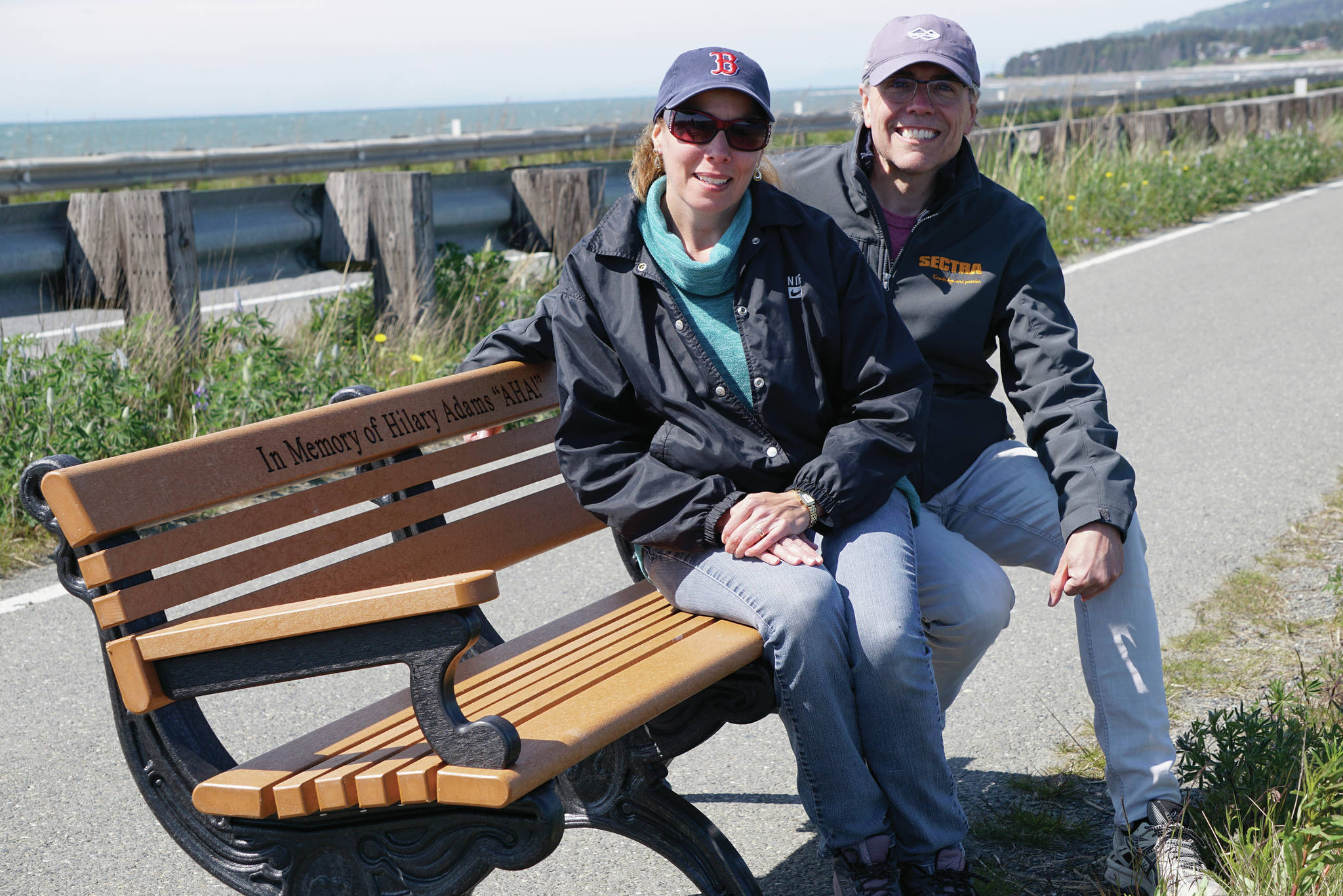 Shell Perretta, left, and David Boissonault, right, sit on a bench on Thursday, June 7, 2021, they donated in memory of Perretta's late mother, Hilary Adams. Homer Parks staff installed the bench on the Homer Spit Trail near the wreck of the Try Again II that day. (Photo by Michael Armstrong/Homer News)