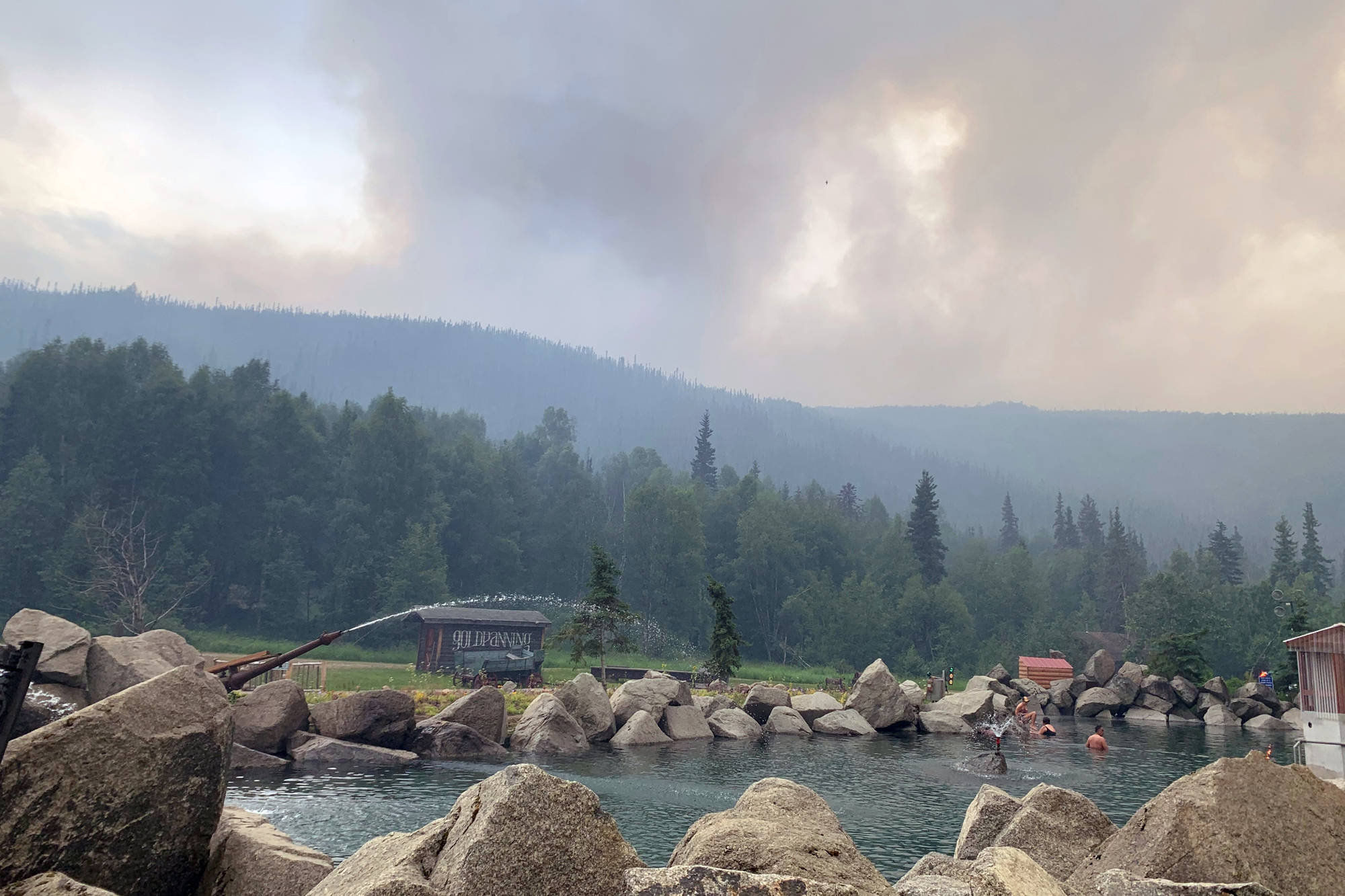 In this photo provided by the Alaska Division of Forestry, smoke from the Munson Creek Fire rises behind the Chena Hot Springs Resort as guests watch from the outdoor rock pool near Fairbanks, Alaska, on Monday, July 5, 2021. Authorities on Monday advised residents and guests at an Alaska hot springs resort to evacuate immediately after a nearby wildfire intensified. The Fairbanks North Star Borough issued the evacuation order when the fire reached a point less than a mile behind Chena Hot Springs. (Alaska Division of Forestry via AP)