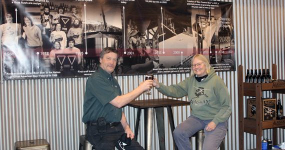 Dana Zigmund / Juneau Empire
Geoff and Marcy Larson toast to 35 years of brewing in the Alaskan Brewing Co. Tap Room on Feb. 4. A timeline of business milestones hangs behind them.