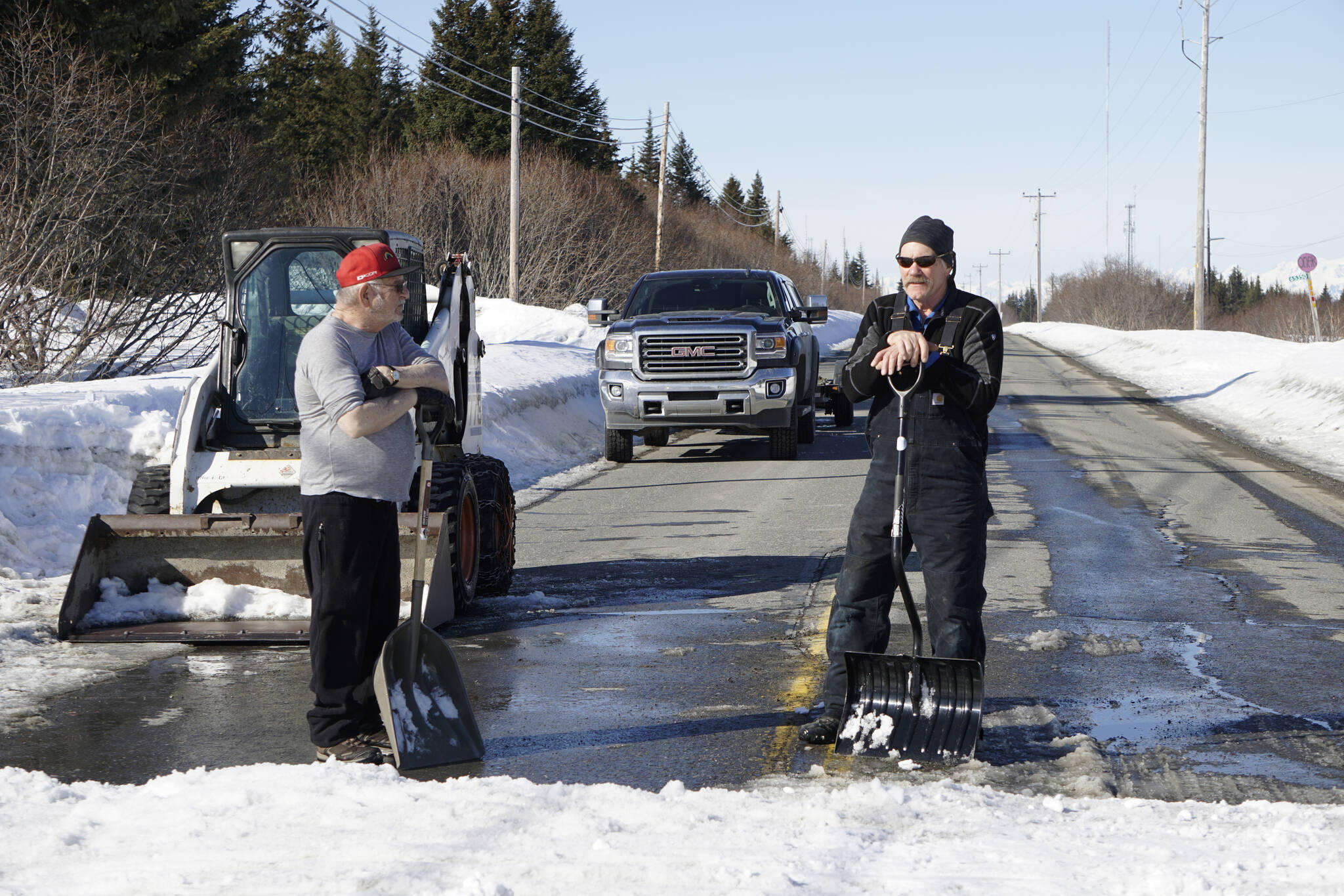 It takes a cosmic village Kachemak Nordic Ski Club volunteers Roy Wilson, left, and Carl Brinkerhoff, right, keep a snow bridge over Diamond Ridge Road in shape for skiers competing in the Kachemak Marathon race on Saturday, March 19, 2022, in Homer, Alaska. (Photo by Michael Armstrong/Homer News)