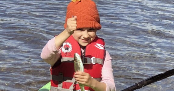 If you teach a kid to fish, she will feed you a trout breakfast every morning of the campout. This proved true for this girl, who holds up a rainbow trout while sitting on a kayak. (Photo by Leah Eskelin)