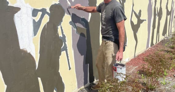 Oregon artist Tom Reed repaints the image of Mark Robinson featured in a mural of Homer performing artists, located in front of Nomar on Pioneer Avenue, on Tuesday, June 11<ins>, 2024, in Homer, Alaska</ins>. (Photo by Emilie Springer/Homer News)