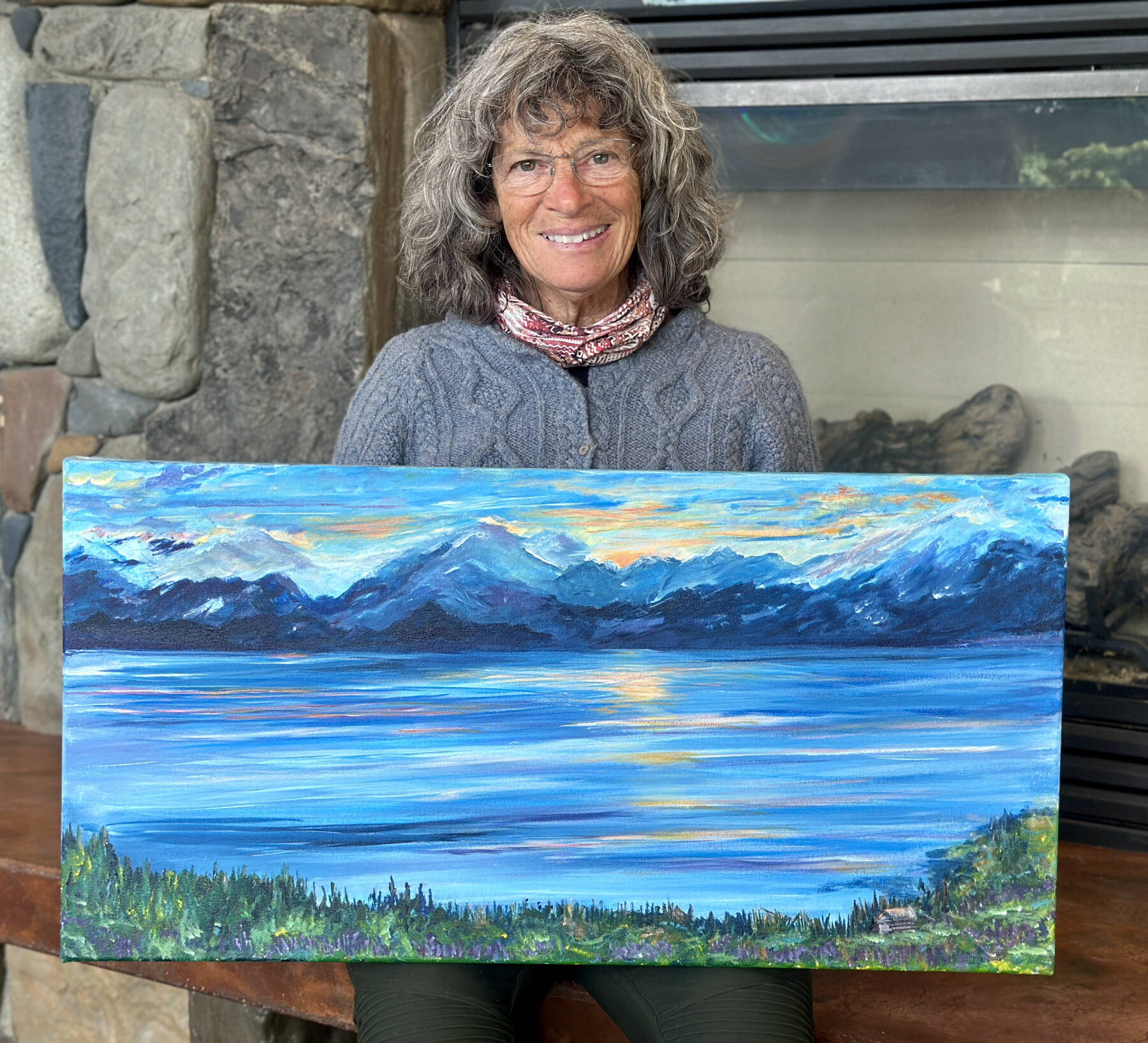 Bonnie Dupree poses with her acrylic painting, “Homestead Sunrise,” on Aug. 8, 2024, where her art is on display through August in the Homer Public Library’s Fireplace Lounge in Homer, Alaska. Photo by Christina Whiting