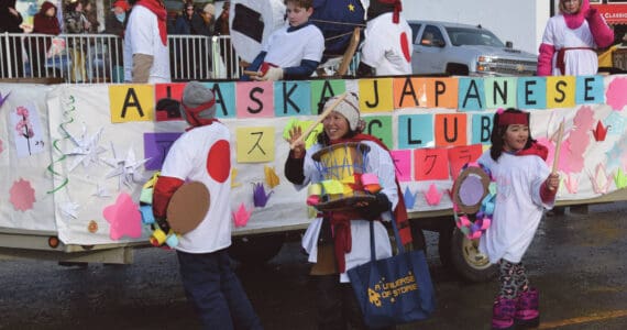 West Homer Elementary School Japanese Club instructor Megumi Beams (center), walking with the Alaska Japanese Club float, carries a cardboard Taiko drum and waves to the crowd at the 70th annual Homer Winter Carnival Parade on Pioneer Avenue on Saturday, Feb. 10, 2024 in Homer, Alaska. (Delcenia Cosman/Homer News)