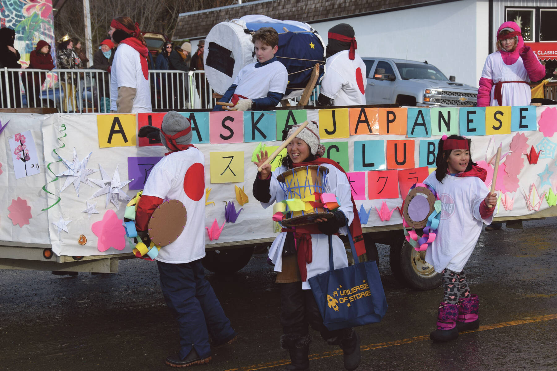 West Homer Elementary School Japanese Club instructor Megumi Beams (center), walking with the Alaska Japanese Club float, carries a cardboard Taiko drum and waves to the crowd at the 70th annual Homer Winter Carnival Parade on Pioneer Avenue on Saturday, Feb. 10, 2024 in Homer, Alaska. (Delcenia Cosman/Homer News)