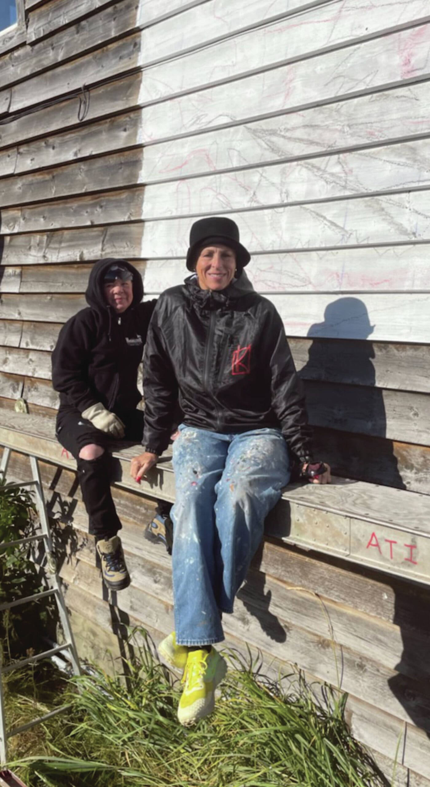 Chicago artist Kathleen Dose-Koehl and assistant RJ Nelson sit in front of the newly sketched mural on the side of a building on Homer Spit Road, ready to begin painting on Monday, Sept. 16, 2024, in Homer, Alaska. Emilie Springer/ Homer News.