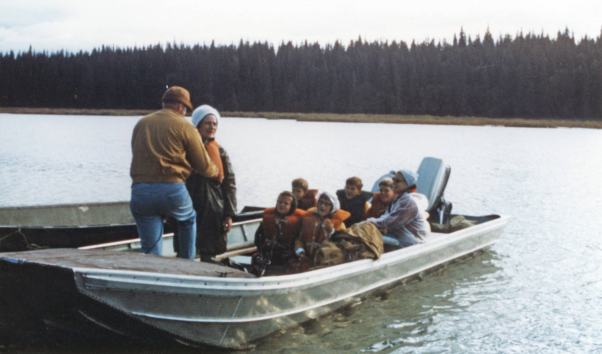 Photo courtesy of the Fair Family Collection
Jane Fair (standing, wearing white hat) receives help with her life jacket from Ron Hauswald prior to the Fair and Hauswald families embarking on an August 1970 cruise with Phil Ames on Tustumena Lake. Although conditions were favorable at first, the group soon encountered a storm that forced them ashore.