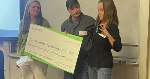 Homer Foundation Executive Director Stacey Schultz, left, receives from Jules and Dawn Ravin an honorary $1.2 million check to support youth in the community at the foundation's annual board meeting at the Kachemak Bay Campus in Homer, Alaska, Nov. 14, 2024. (Photo by Emilie Springer/Homer News)