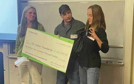 Homer Foundation Executive Director Stacey Schultz, left, receives from Jules and Dawn Ravin an honorary $1.2 million check to support youth in the community at the foundation's annual board meeting at the Kachemak Bay Campus in Homer, Alaska, Nov. 14, 2024. (Photo by Emilie Springer/Homer News)