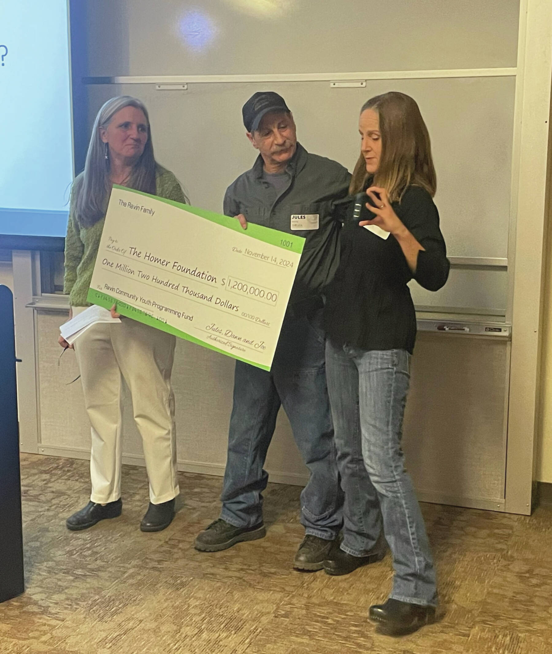 Photo by Emilie Springer/Homer News
Homer Foundation Executive Director Stacey Schultz, left, receives from Jules and Dawn Ravin an honorary $1.2 million check to support youth in the community at the foundation’s annual board meeting at Kachemak Bay Campus, Nov. 14.