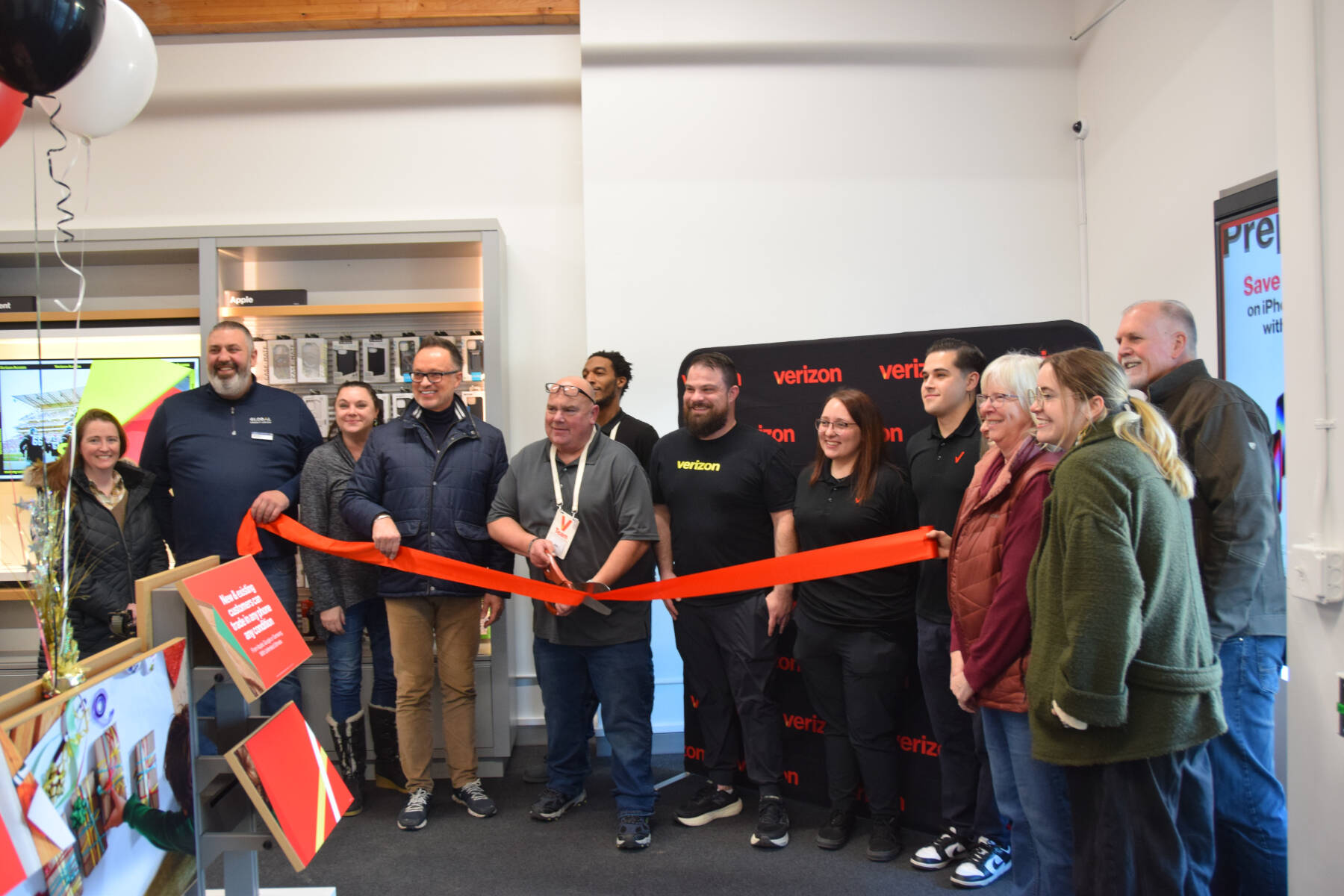 General manager John Fromm (center), Victra Homer employees, Homer Chamber of Commerce staff and board members, and City of Homer staff attend a ribbon cutting ceremony during Victra’s grand opening on Thursday, Nov. 21, 2024, in Homer, Alaska. (Delcenia Cosman/Homer News)