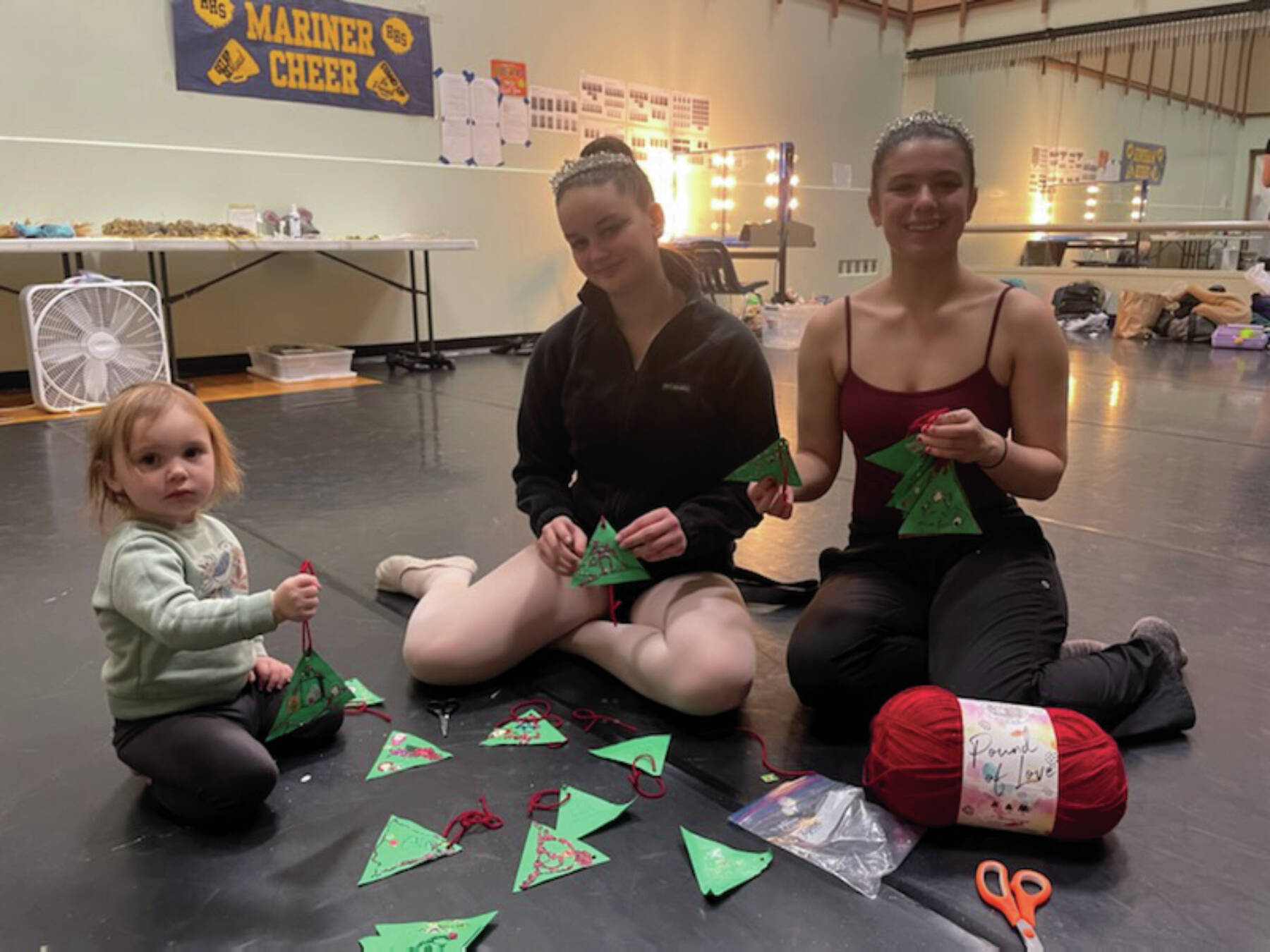 Homer “Nutcracker” dancers Ella Gustufson and Sofia Loboy help create Christmas tree gift tags for the 2024 Homer Share the Spirit in the Homer High School green room during “Nutcracker” rehearsal last weekend. They are joined by one of the Nutcracker’s small participants. (Emilie Springer/Homer News)