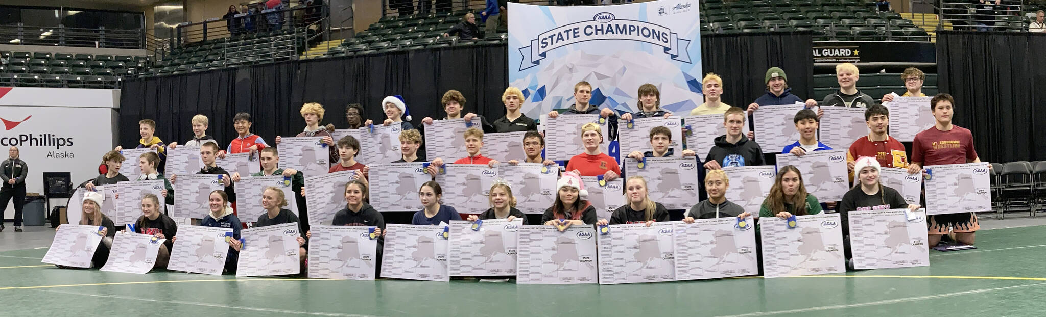 All of the individual champions, with the girls in the front, Division II wrestlers in the middle, and Division I winners in the back, pose with their brackets at the state wrestling tournament Saturday, Dec. 21, 2024, at the Alaska Airlines Center in Anchorage, Alaska. (Photo by Jeff Helminiak/Peninsula Clarion)