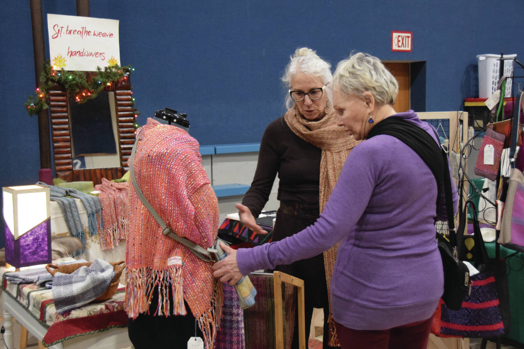 Bonita Banks (rear) talks with a patron at her booth, sit.breathe.weave handwovens, at the Procrastinators Fair on Saturday, Dec. 21<ins>, 2024,</ins> at Christian Community Church in Homer<ins>, Alaska</ins>. (Delcenia Cosman/Homer News)