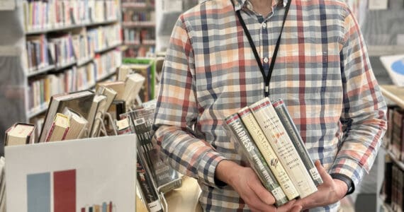 Matthew Smith, Homer Public Library staff member and the organizer for the annual Lit Lineup community reading program, poses with a selection of books next to the lineup display on Friday, Jan. 3, 2025, in Homer, Alaska. Photo by Christina Whiting