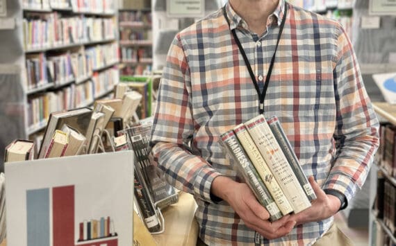 Matthew Smith, Homer Public Library staff member and the organizer for the annual Lit Lineup community reading program, poses with a selection of books next to the lineup display on Friday, Jan. 3, 2025, in Homer, Alaska. Photo by Christina Whiting